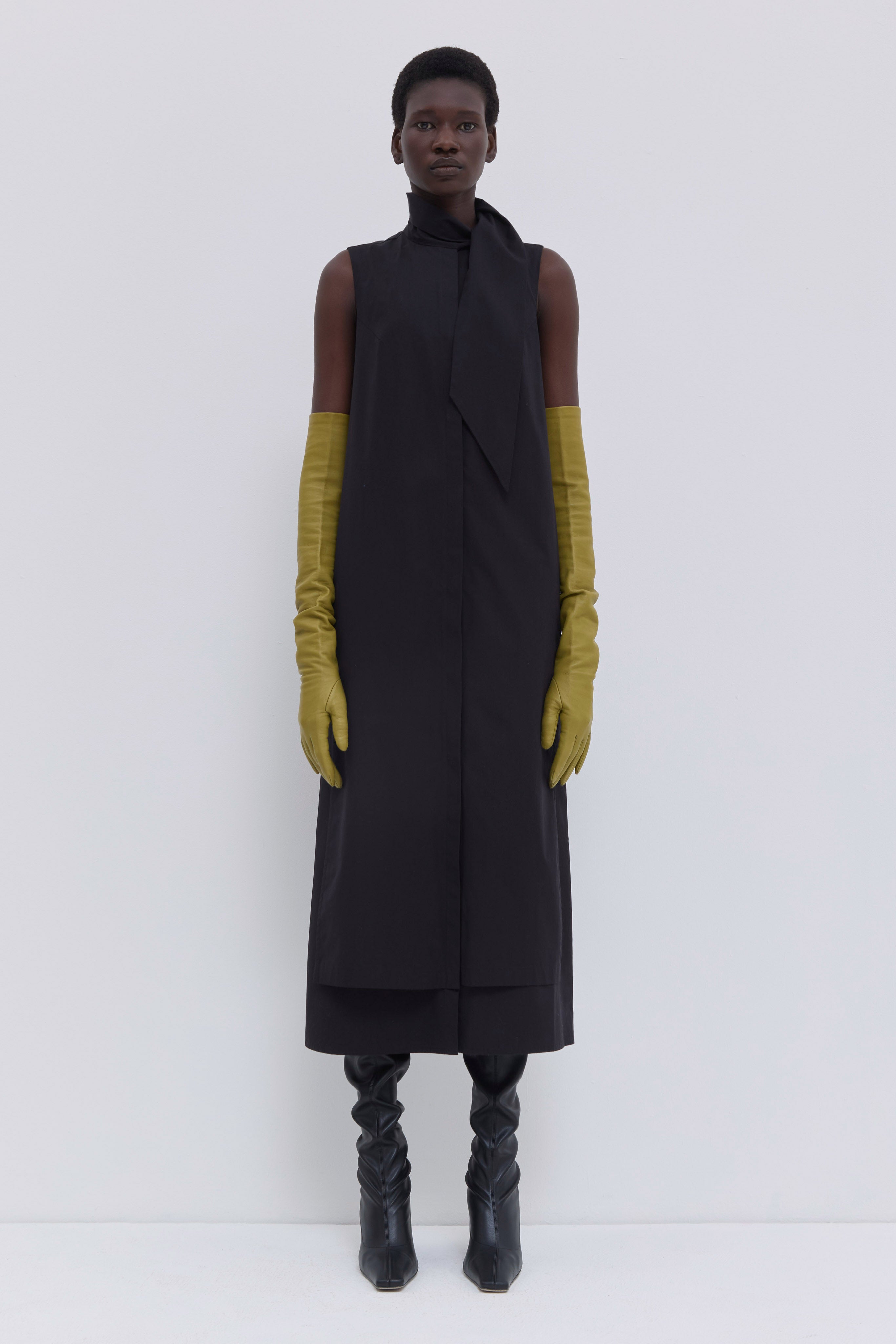 Model wearing a black sleeveless cotton dress with asymmetric scarf detail, layered construction and midi length by Christian Wijnants.
