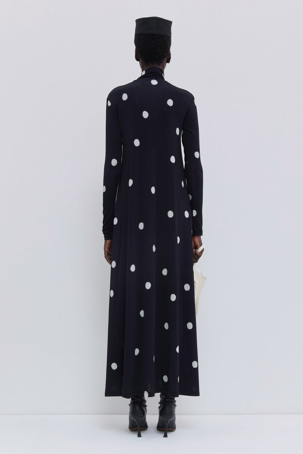 Back view of a black maxi jersey dress featuring a large white dot print, long sleeves and flowing silhouette by Christian Wijnants.