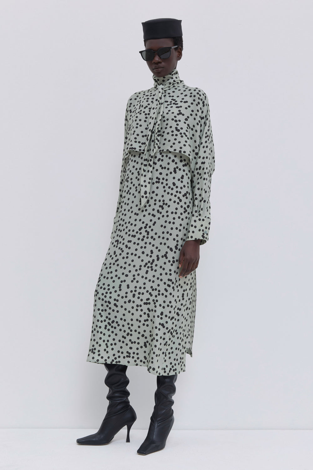 Side view of a sage polka dot dress featuring batwing sleeves, scarf detail and fluid drape by Christian Wijnants.