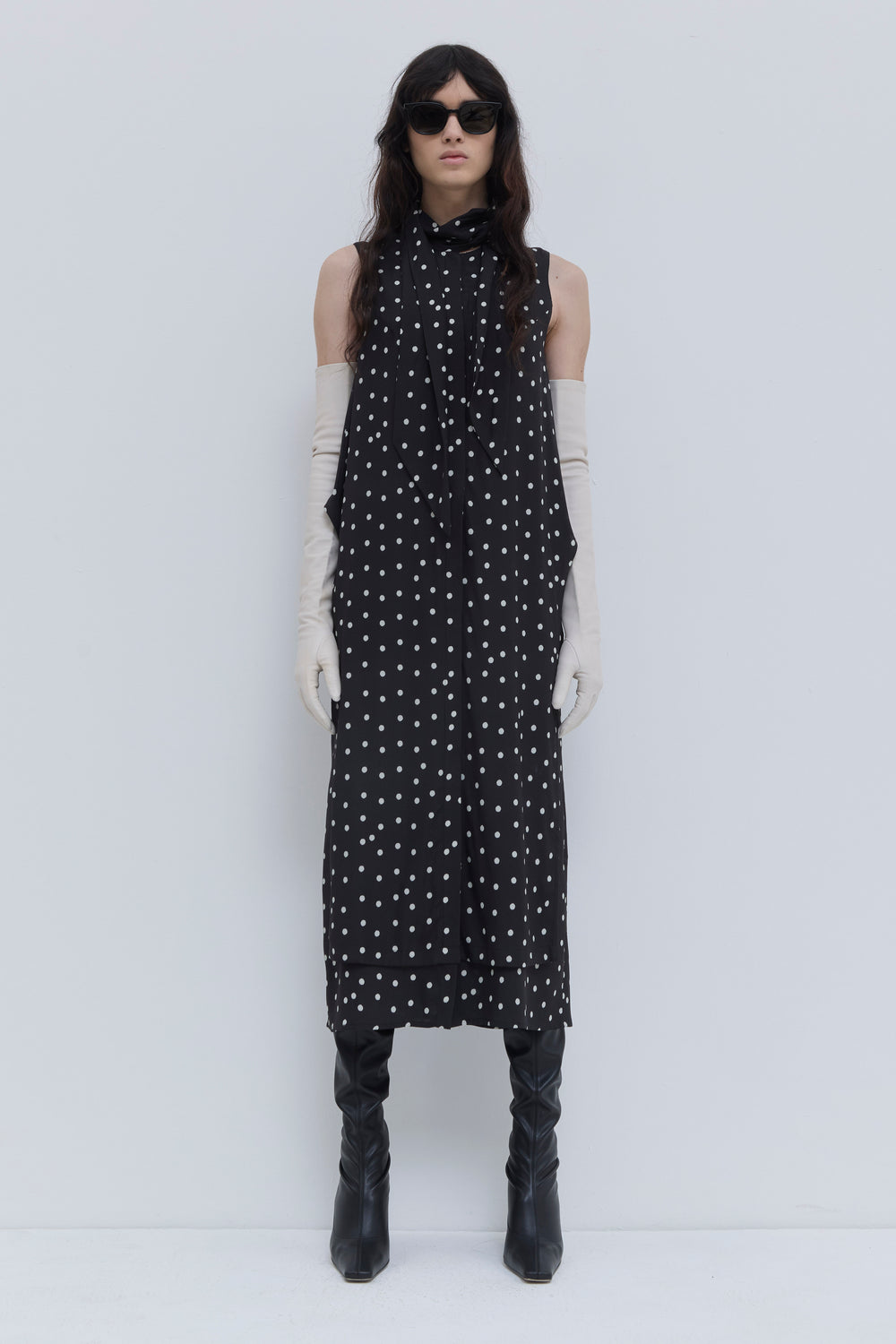 Model wearing a black dotted sleeveless midi dress with asymmetric scarf detail, side pockets and layered silhouette by Christian Wijnants.