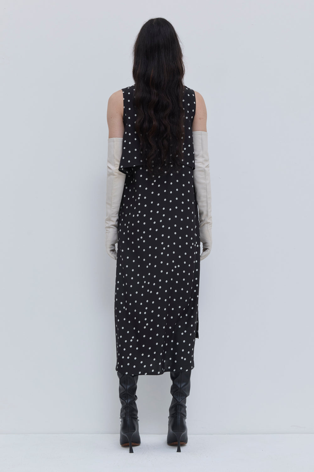 Back view of a black dotted midi dress featuring a layered silhouette, sleeveless cut and flowing drape by Christian Wijnants.