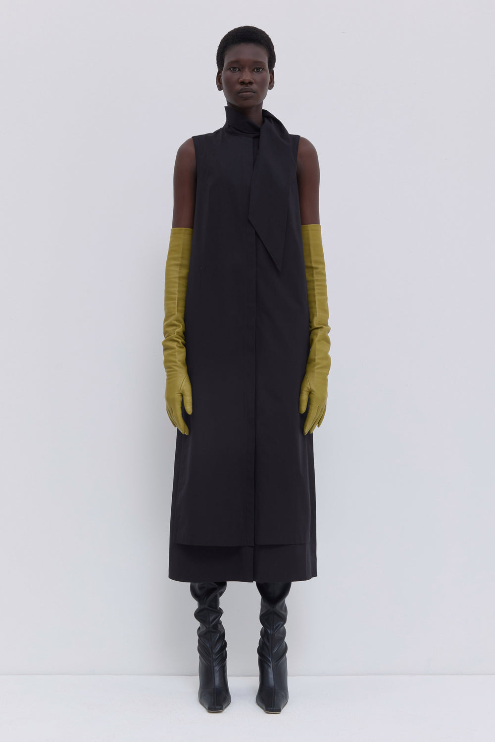 Model wearing a black sleeveless cotton dress with asymmetric scarf detail, layered construction and midi length by Christian Wijnants.
