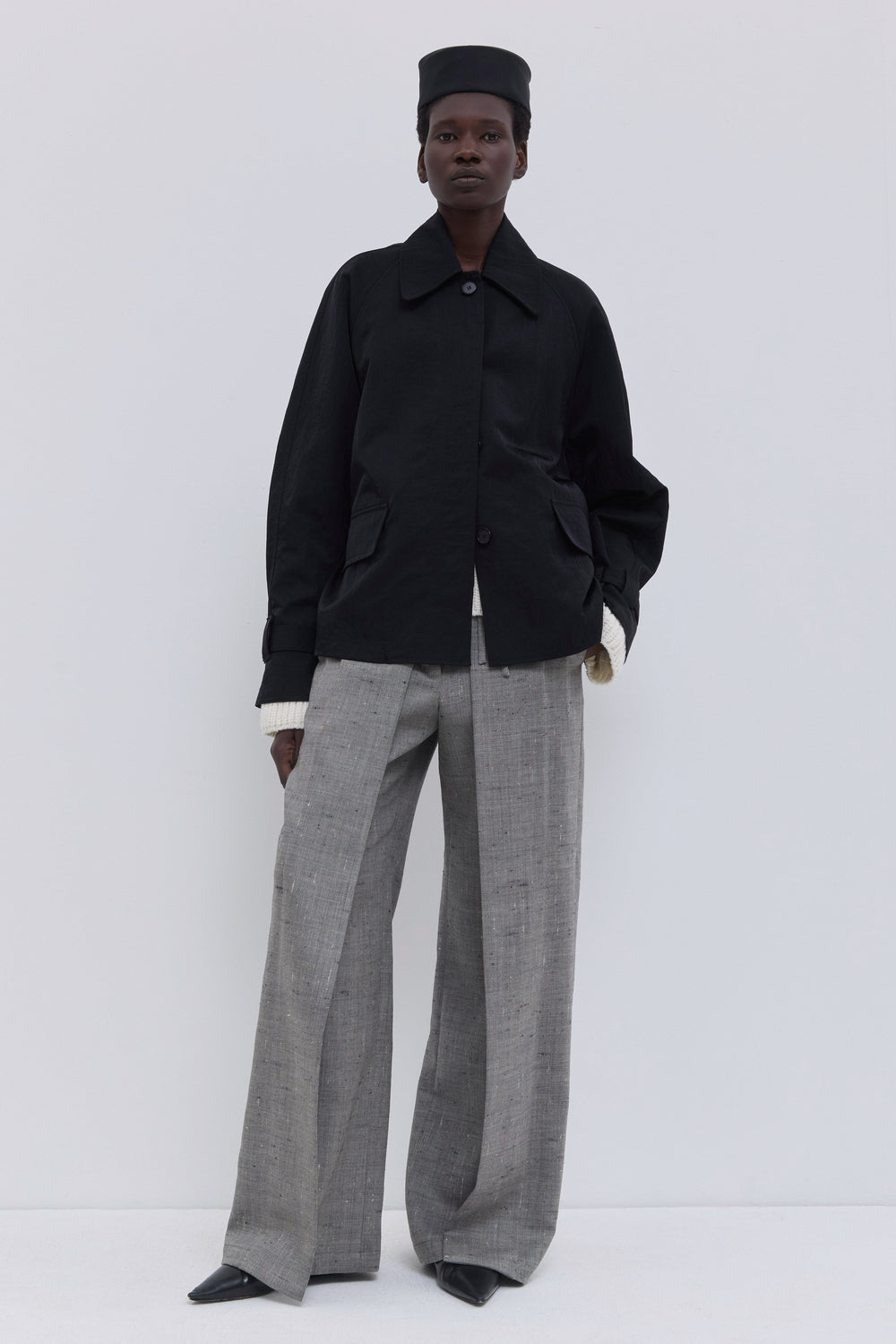 Black woven jacket with oversized pockets styled over knitwear and tailored trousers.