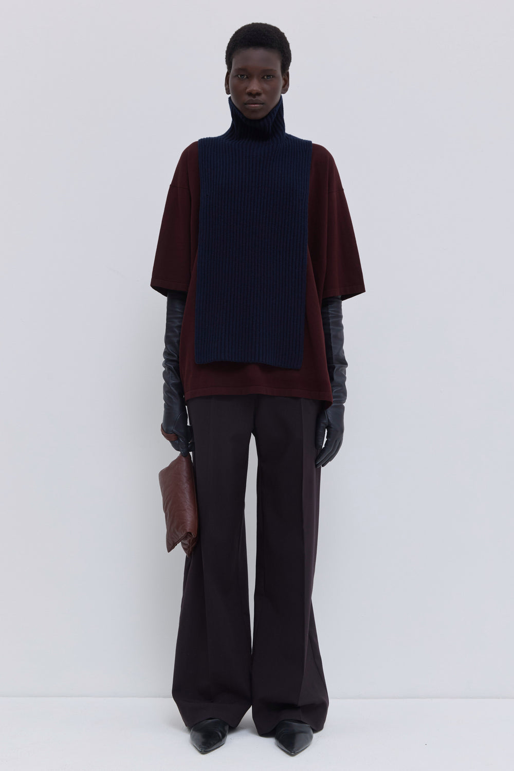 Dark marine ribbed merino wool and cashmere knit bib with oversized turtleneck, layered over a burgundy T-shirt and tailored trousers.