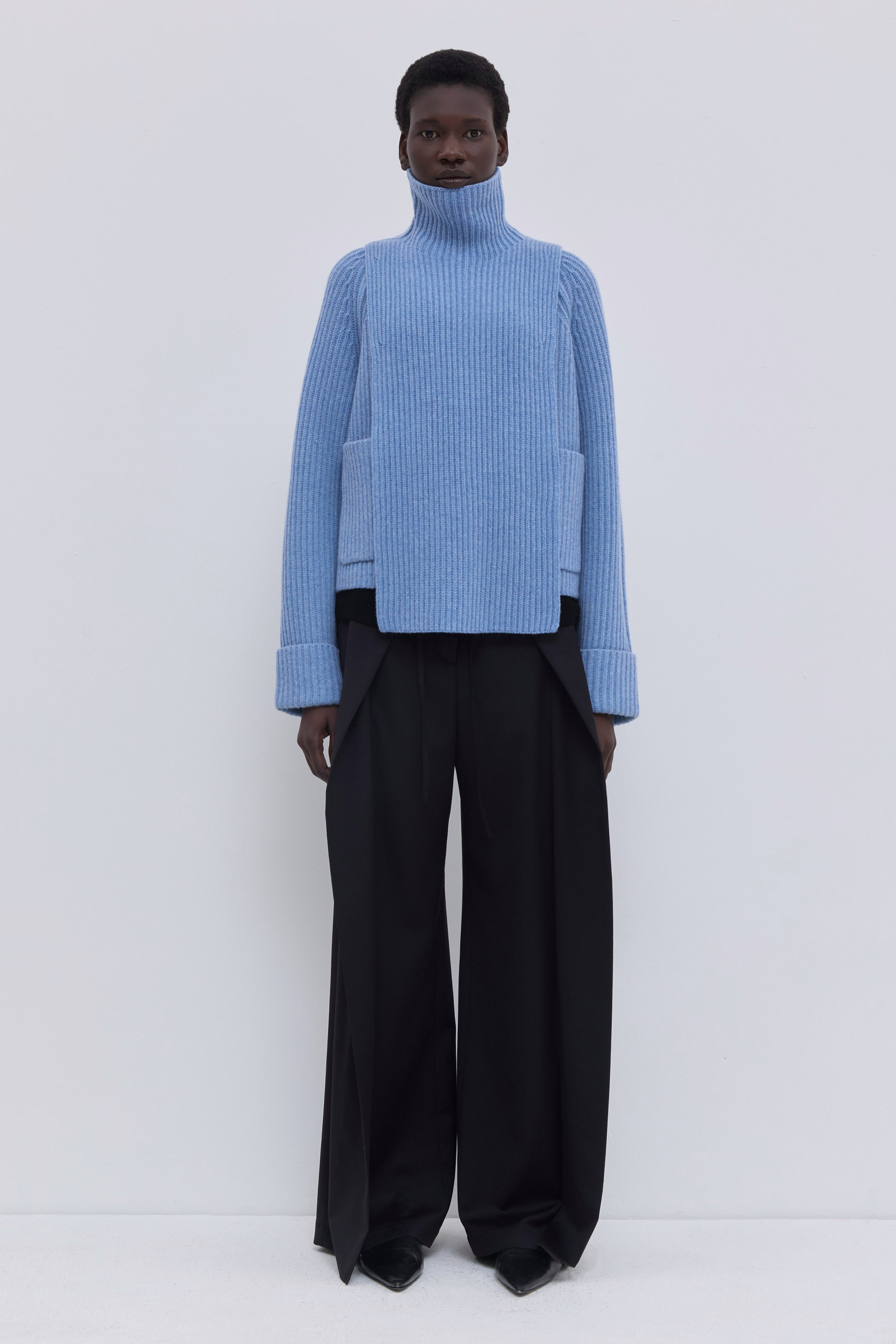 Mirage blue ribbed merino wool and cashmere knit bib with oversized turtleneck, layered under a cropped blazer with tailored wide-leg trousers.