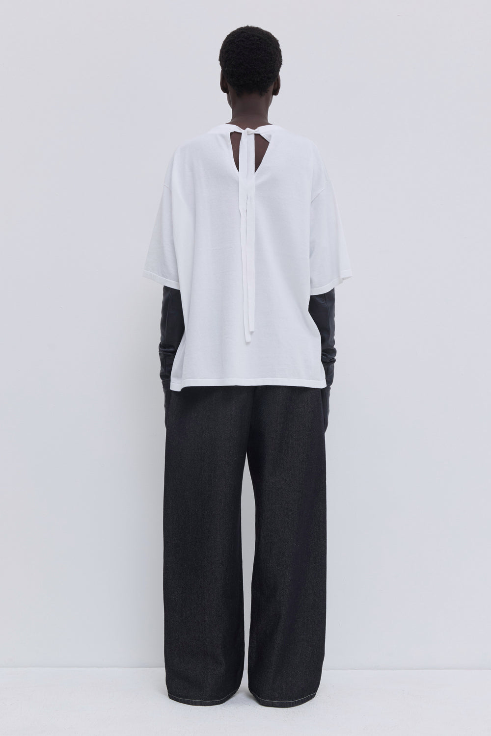 Back view of a white jersey T-shirt featuring an open back with strap closure.