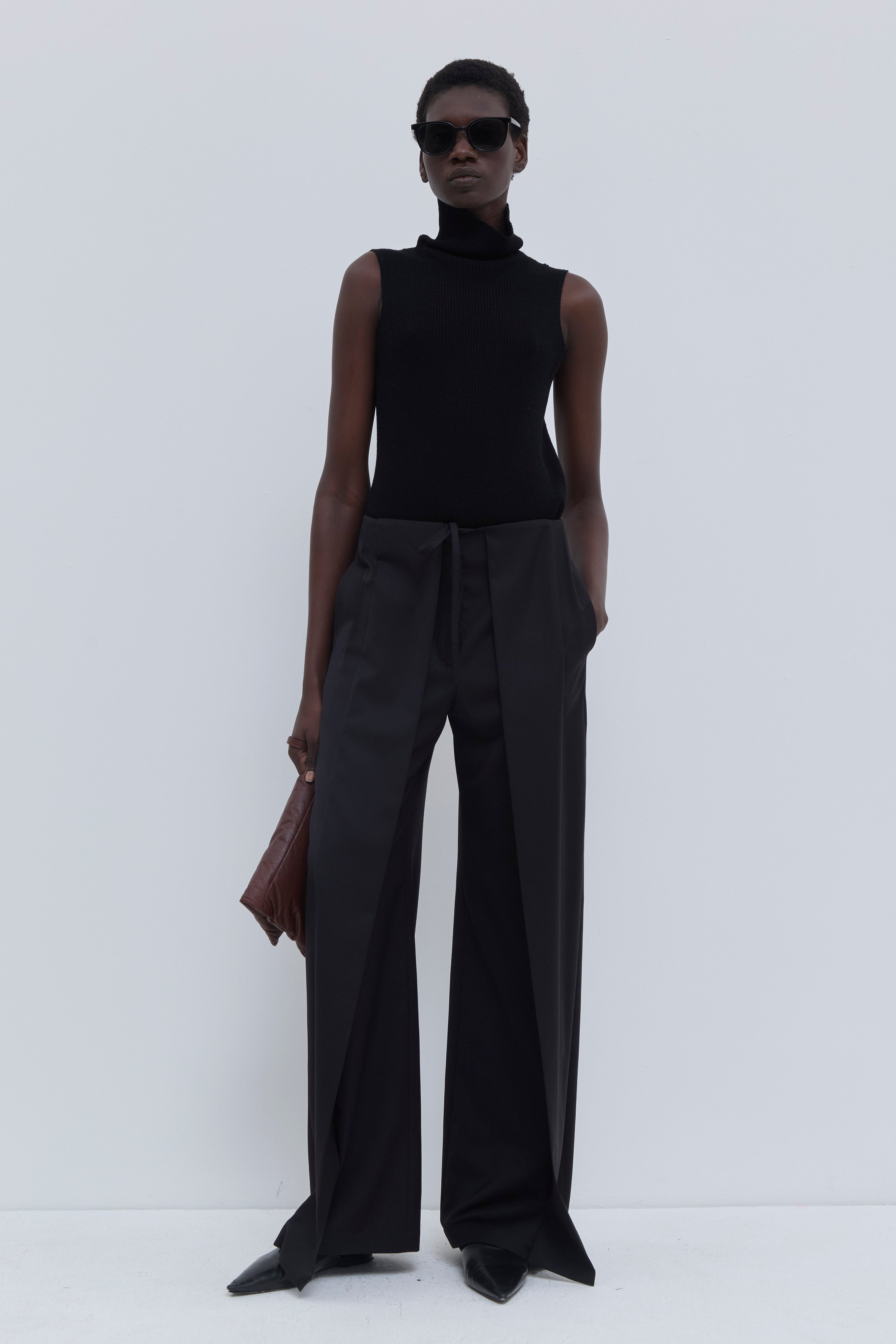 Front view of the Paire wide-leg trousers in black styled with a sleeveless knit top and leather clutch.