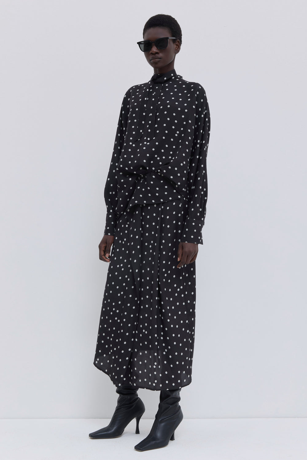 Back view of a black polka dot skirt with fluid drape, elastic waistband and asymmetric silhouette by Christian Wijnants.