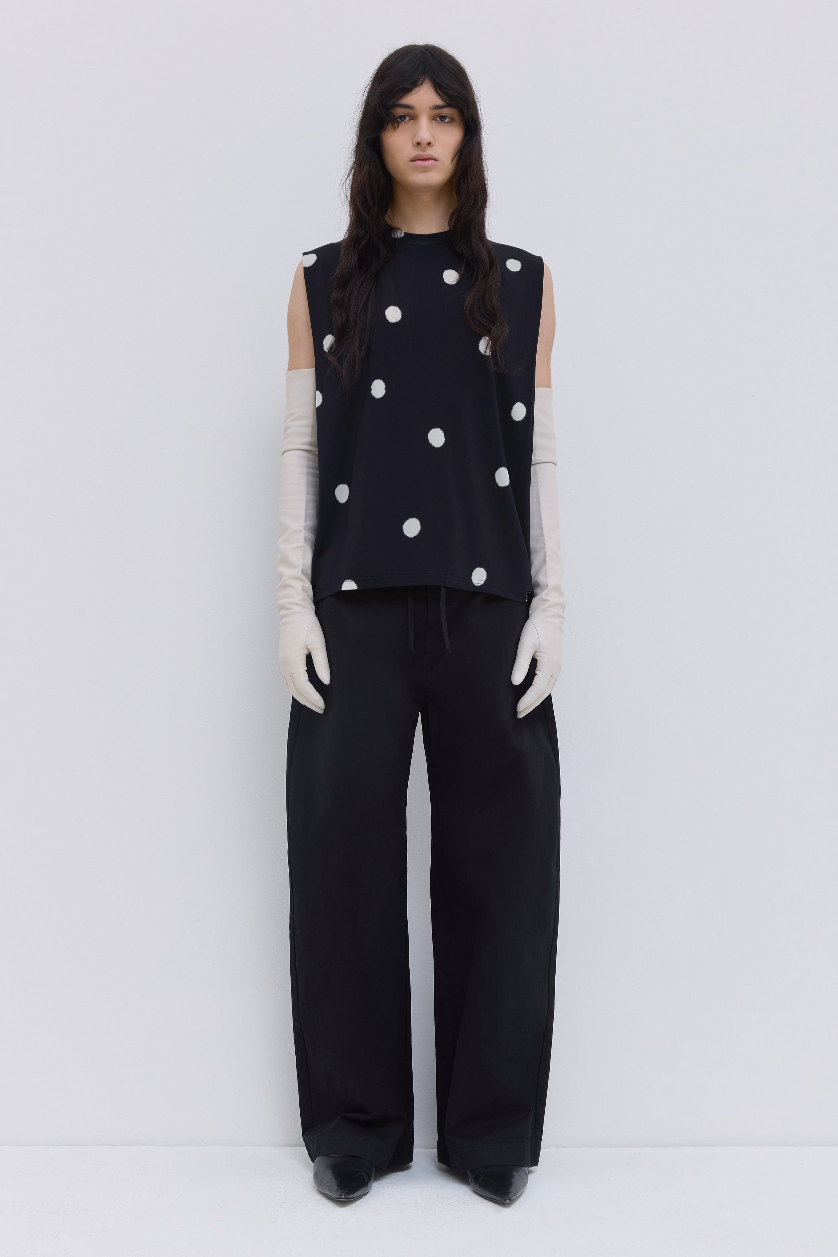 Model wearing a black sleeveless jersey top with large white polka dot print, shoulder pleat detail and relaxed fit by Christian Wijnants.