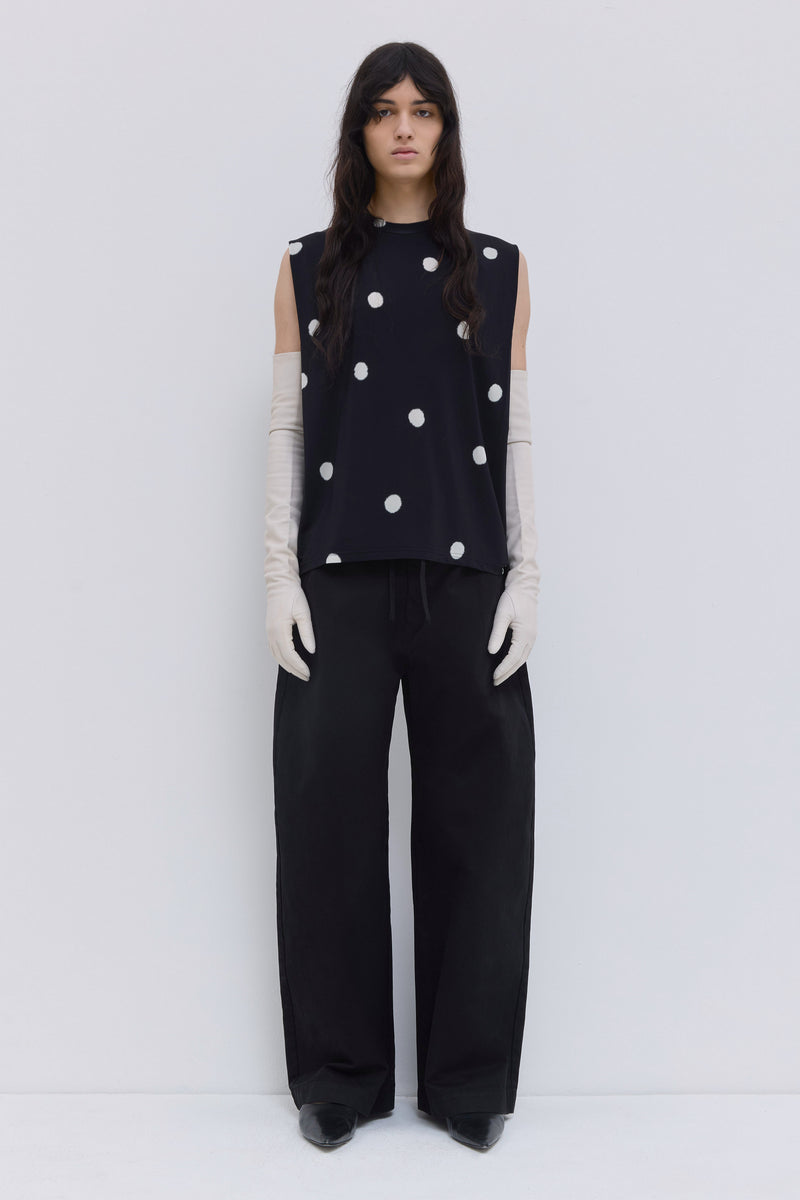 Model wearing a black sleeveless jersey top with large white polka dot print, shoulder pleat detail and relaxed fit by Christian Wijnants.