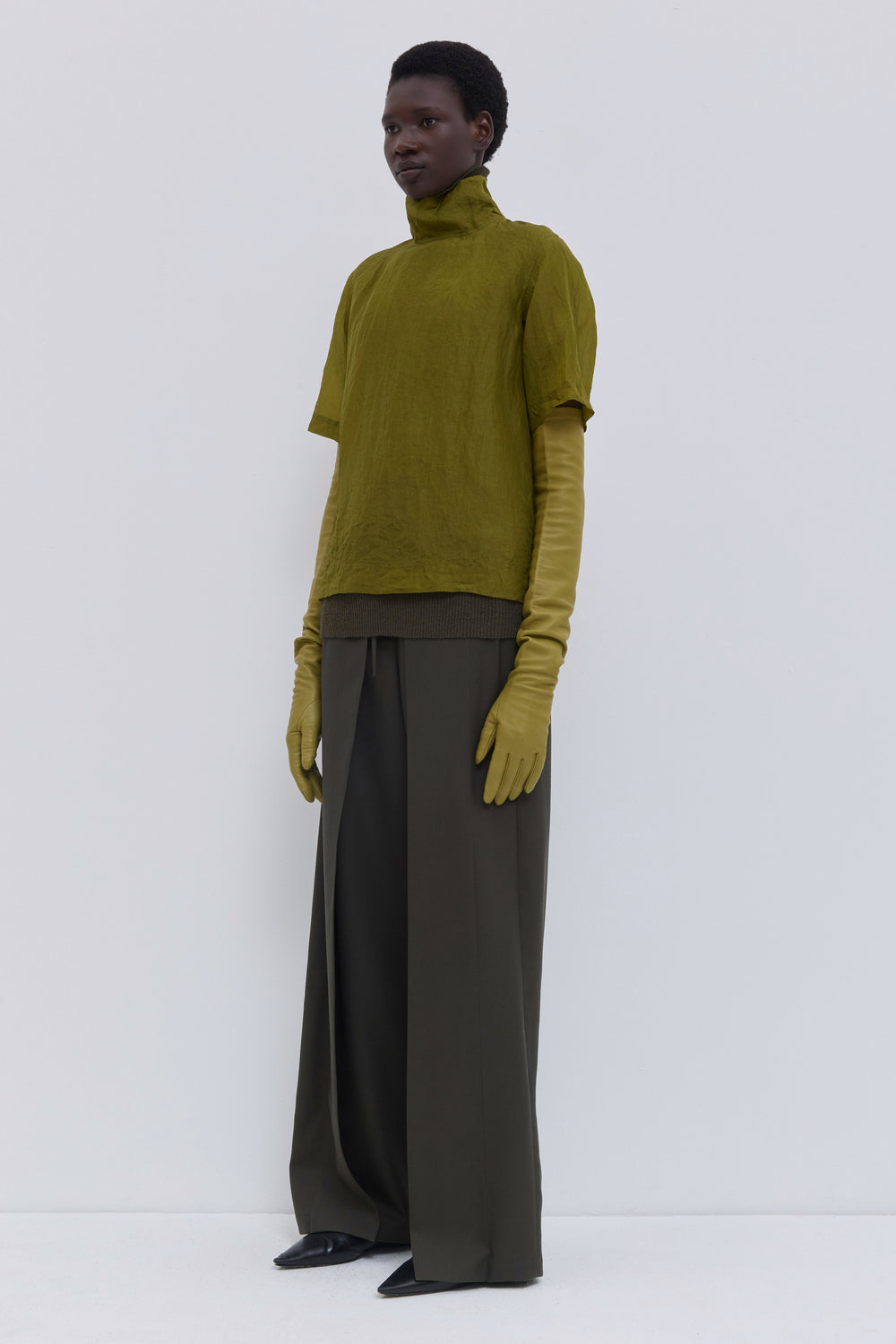 Side view of the Tapulo high-neck top in olive silk organza featuring a button closure and handcrafted crinkled finish.