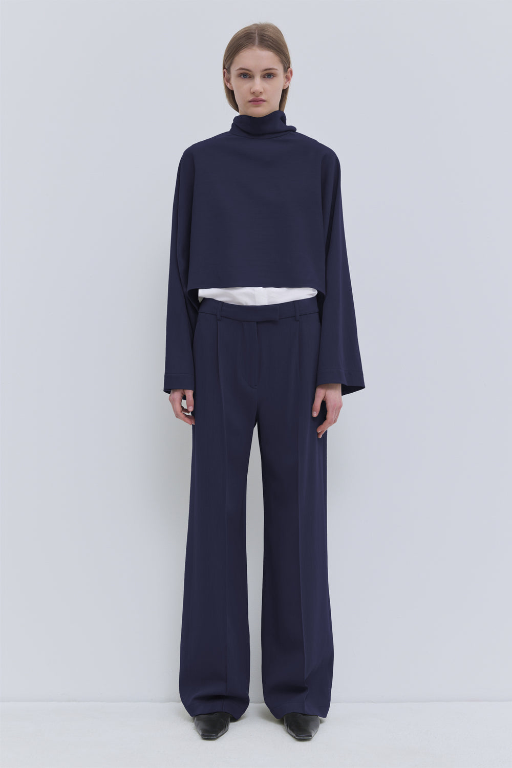 Dark navy cropped wool top with high neckline and draped scarf detail, front view.